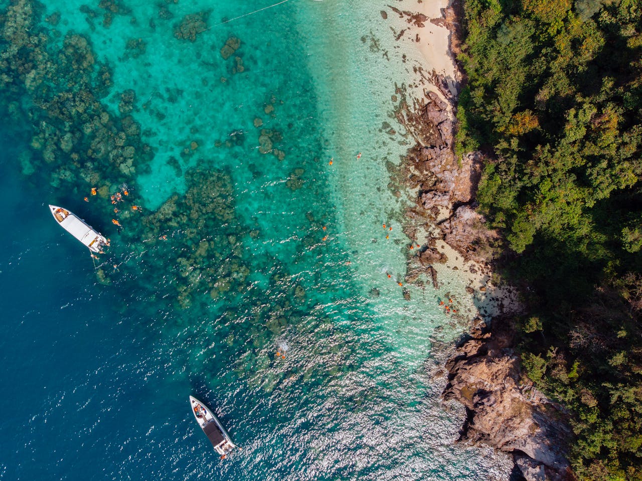 Drone shot capturing the vibrant blue waters, boats, and lush greenery on a tropical beach.
