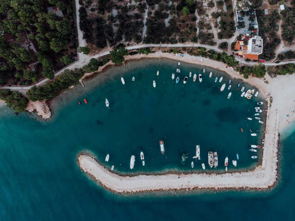 Aerial view of boats docked in a serene turquoise bay, surrounded by lush greenery and rocky shores.