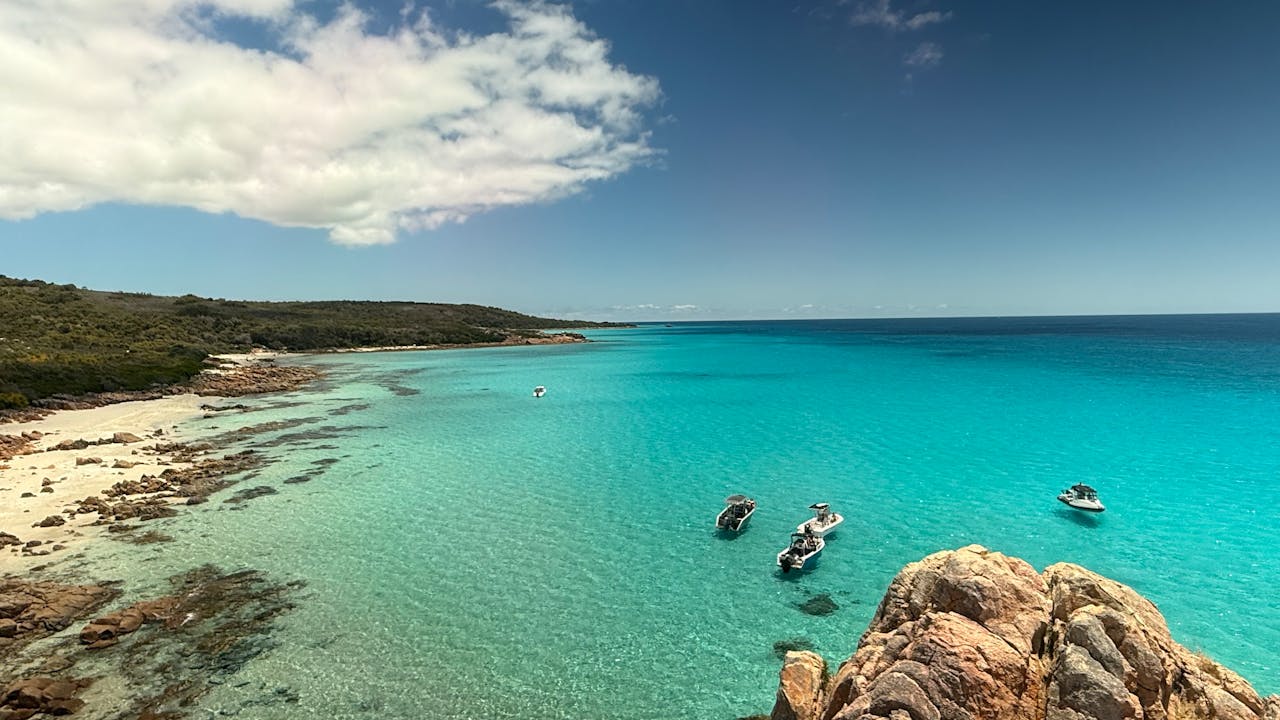 Services-03 Aerial view of a stunning coastal landscape with boats on crystal clear blue waters.